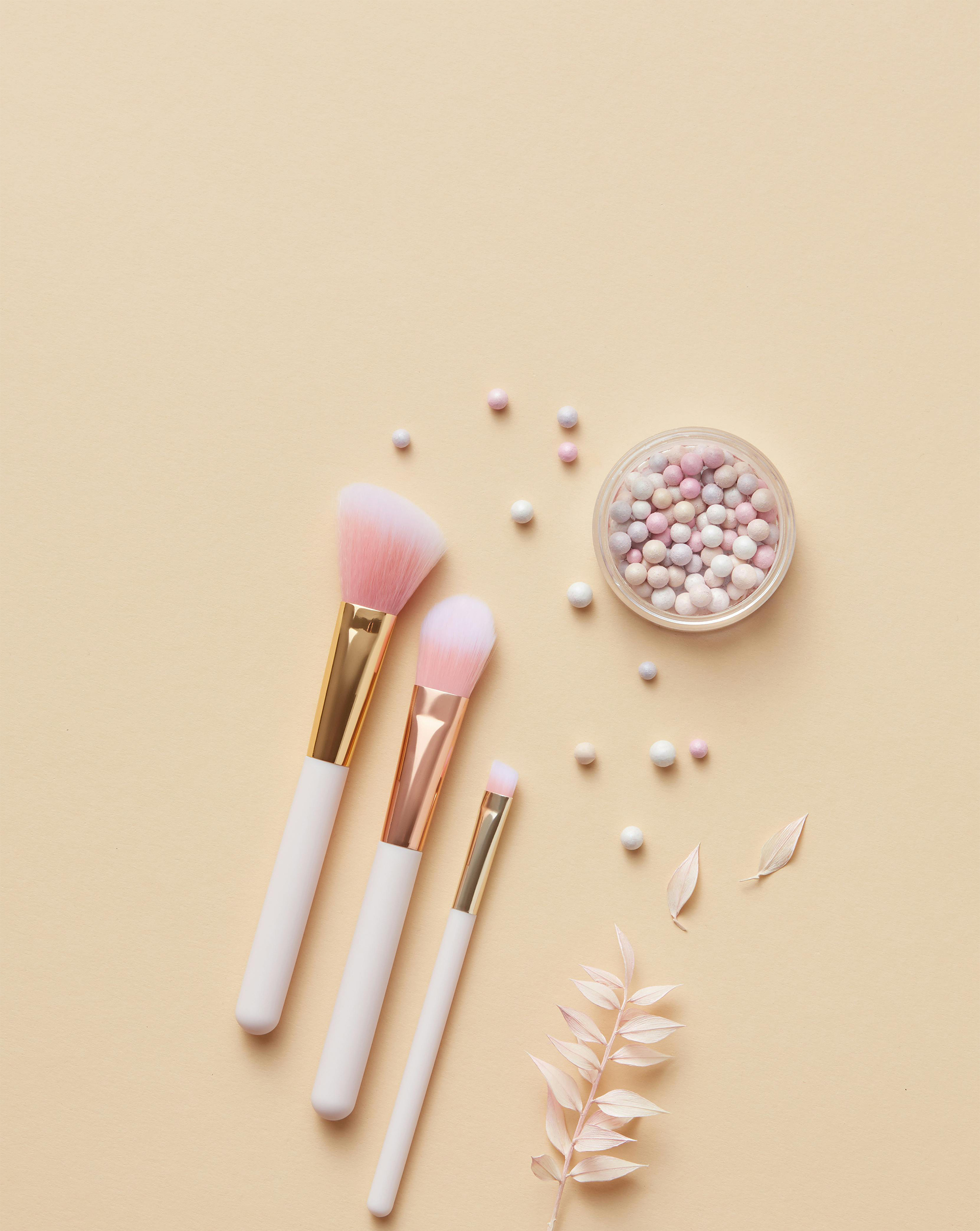 Makeup brushes with a small container of pearls on a beige background